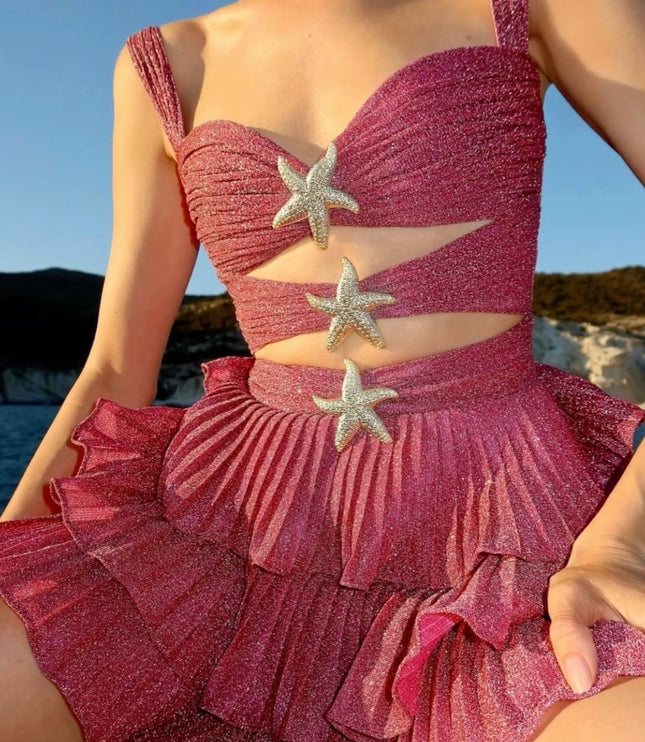 Women's shimmery coral summer mini dress with cut-outs and silver starfish details, worn outdoors.