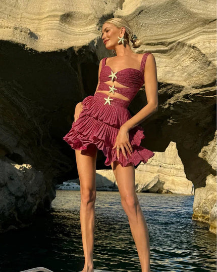 Woman in a shimmery coral summer mini dress with cut-outs and gold starfish details, posing on a boat.