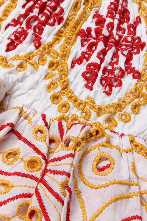 Close up of the transition from shirred bodice to tiered skirt on a women's embroidered mini dress, showcasing the red and yellow designs.