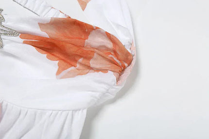 Close-up detail of the orange floral print and ruched bust on the white halter mini dress.