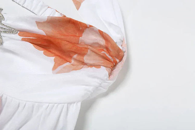 Close-up detail of the orange floral print and ruched bust on the white halter mini dress.