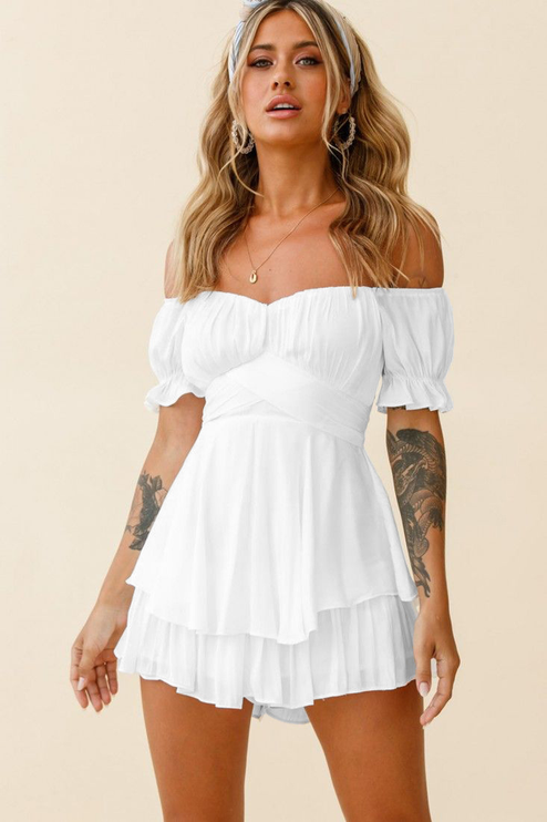 Front view of a white off-shoulder tiered ruffle romper, with a sweetheart neckline, short puffed sleeves, and a crossover waist.