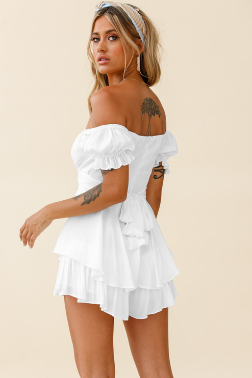 Back 3/4 view of a white off-shoulder summer romper, highlighting the tiered ruffles, tie-back detail, and short length.