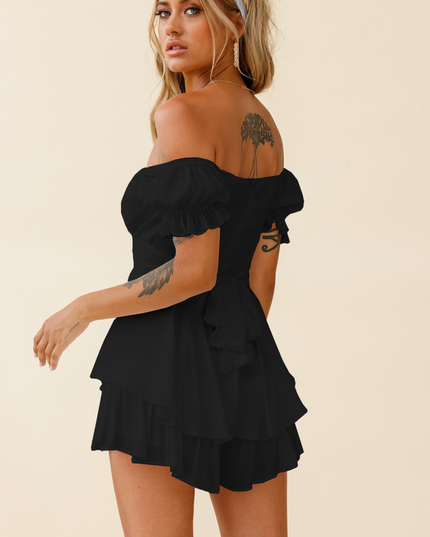 Back 3/4 view of a black off-shoulder summer romper, showcasing the layered ruffles, tie-back closure, and short hemline.