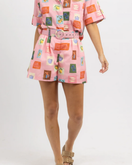 Front view of women's pink summer short set with a playful fruit and vase print, paired with gold slides.