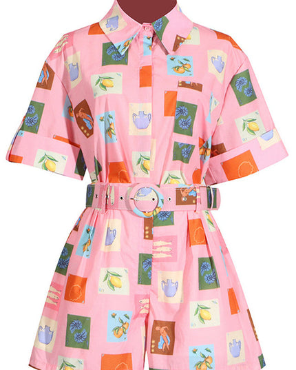 Flat lay of pink short sleeve shirt and shorts set with a unique fruit and vase pattern and a matching belt.