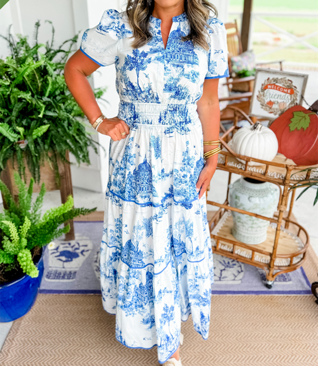 Women's white summer maxi dress featuring blue scenic print, v-neck, short sleeves, tiered skirt, and smocked waist, with white slides.