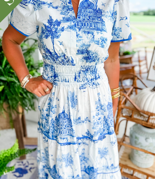 Close-up of women's white summer maxi dress in blue scenic print, showing v-neckline, smocked waist, and tiered skirt detail.