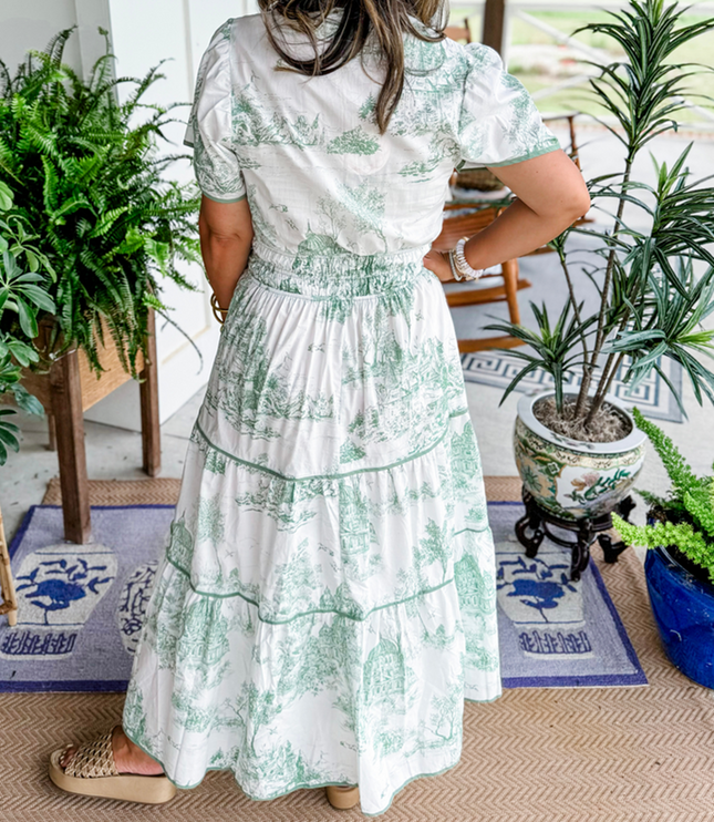Back view of women's white summer maxi dress with light green scenic print, short sleeves, and smocked waist, with platform slides.