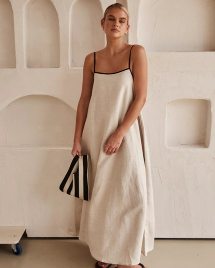 Full length view of a women's sleeveless maxi dress in light beige, with striped clutch.