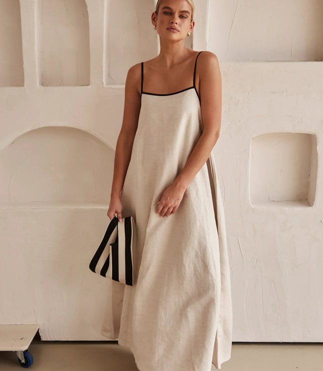 Full length view of a women's sleeveless maxi dress in light beige, with striped clutch.