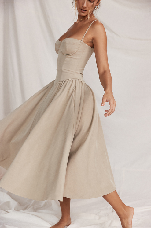 Side view of a women's light beige sweetheart neck corset midi dress, showcasing the gathered waist and movement of the skirt.