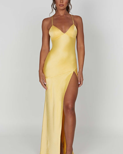 Full-length view of a women's bright yellow satin maxi dress with a V-neck, thin straps, and a high side slit, paired with nude square-toe slides.