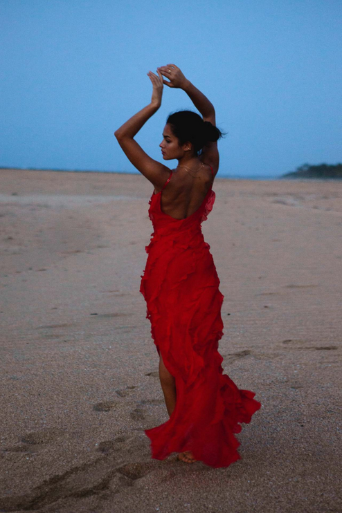 Full length view of a red V-neck ruffle side slit maxi dress with spaghetti straps on a beach at dusk