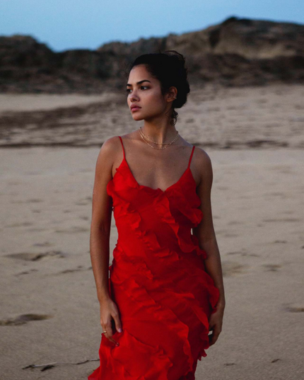 Close up of a red V-neck ruffle side slit maxi dress with delicate spaghetti straps on a beach