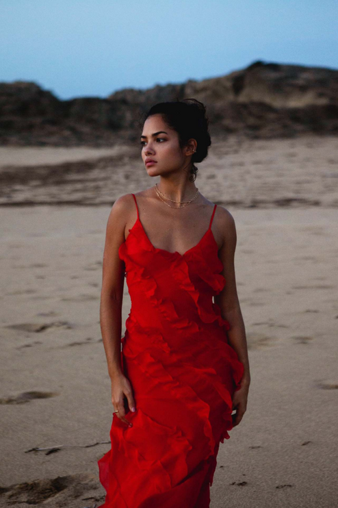 Close up of a red V-neck ruffle side slit maxi dress with delicate spaghetti straps on a beach