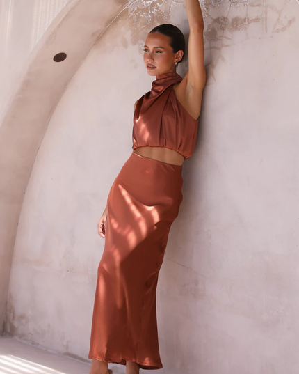 Full length view of a women's rust orange satin high neck crop top and maxi skirt set, with arm raised, suitable for wedding guests.
