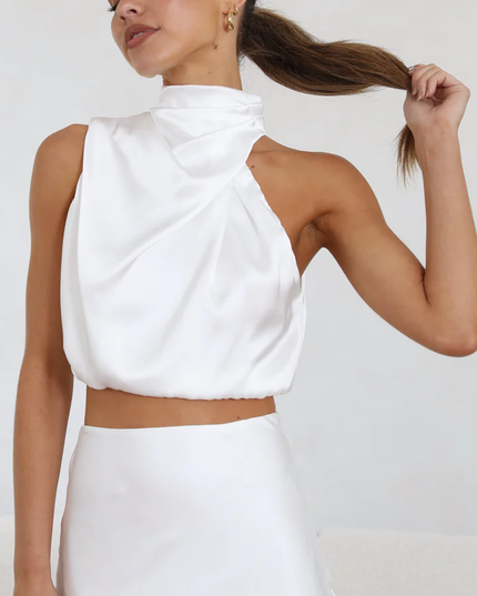Close-up of women's white satin asymmetrical high neck crop top from a two-piece maxi dress set, with subtle pleating.