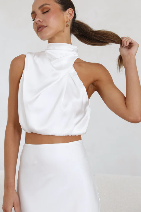 Close-up of women's white satin asymmetrical high neck crop top from a two-piece maxi dress set, with subtle pleating.
