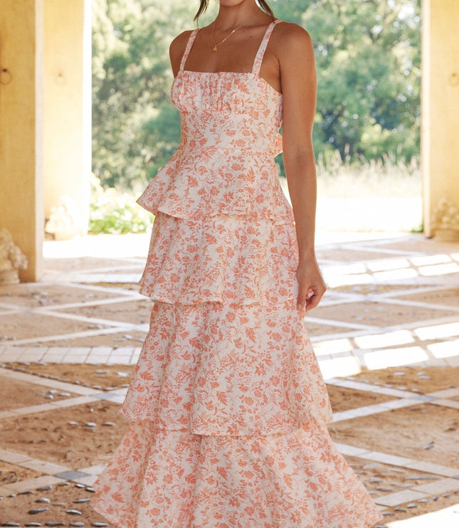 Full-length view of a woman in the pink floral ruffled maxi dress, smiling and standing in an arched hallway.