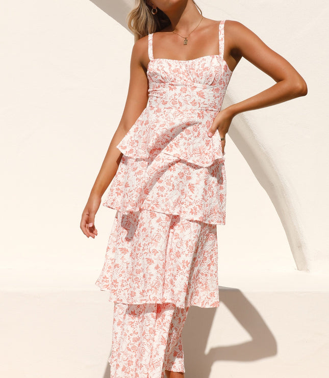 Woman posing confidently in the pink floral ruffled maxi dress, with hands on hips against a white wall.