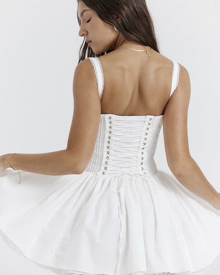 Back view of the white corset lace-up mini dress, with the model turning to reveal the full lace-up detail and ruffled skirt.