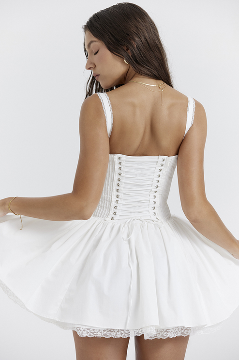 Back view of the white corset lace-up mini dress, with the model turning to reveal the full lace-up detail and ruffled skirt.