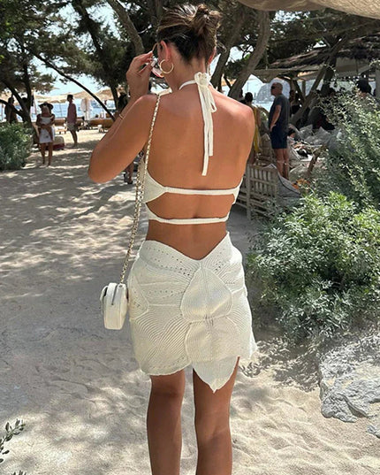 Back view of a women's white crochet halter neck mini dress, showcasing the open back and unique skirt design.