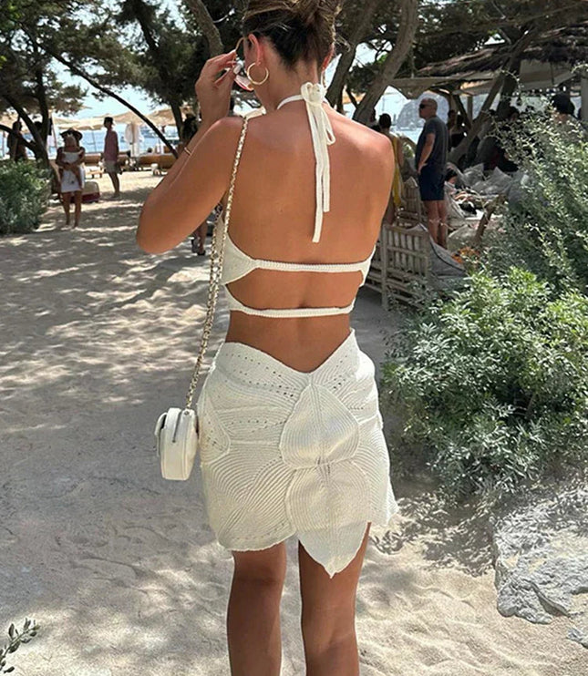 Back view of a women's white crochet halter neck mini dress, showcasing the open back and unique skirt design.