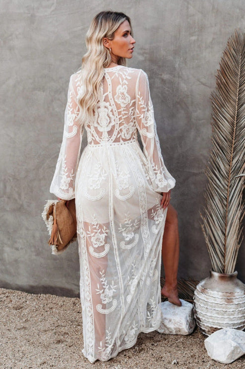 Back view of a white lace maxi dress, showcasing the sheer long sleeves and detailed floral embroidery on the back.