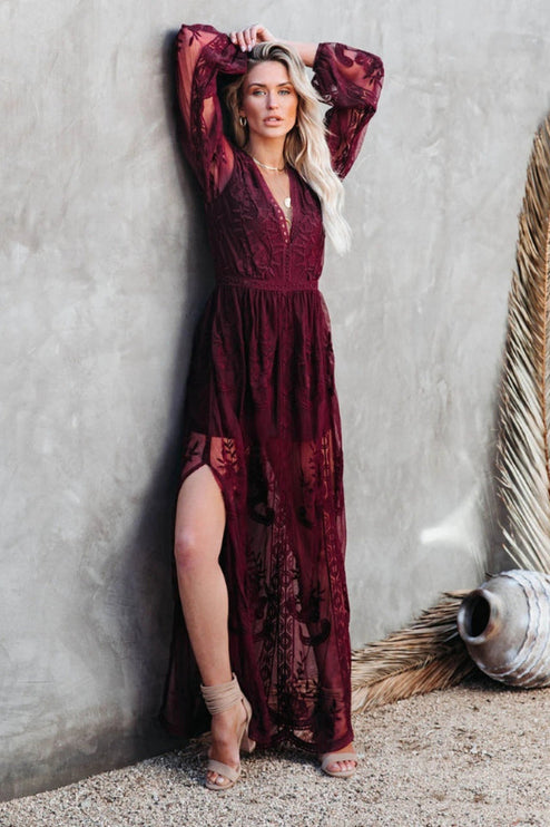 Side view of a burgundy lace long sleeve V-neck maxi dress, featuring a high slit and delicate floral patterns.