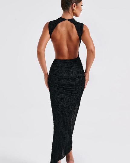 Back view of a black sleeveless mock neck midi dress with a daring open back and textured fabric, paired with black heels.