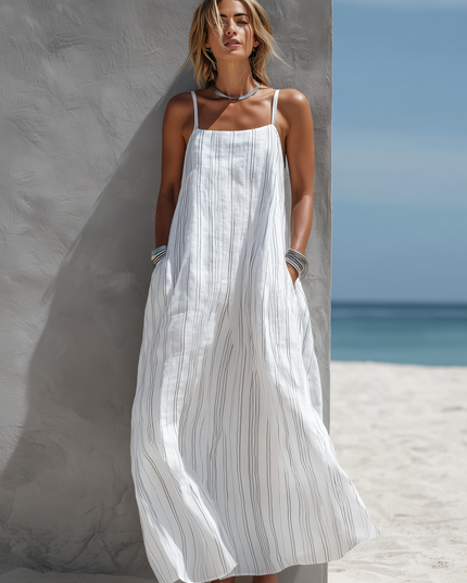 Full body view of women's white striped sleeveless maxi dress with spaghetti straps and side pockets, on sand.